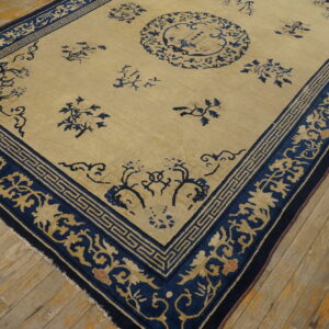 Beige field rug with a dark blue border and scattered floral designs lies on distressed wood flooring.