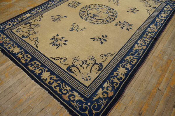 Beige field rug with a dark blue border and scattered floral designs lies on distressed wood flooring.
