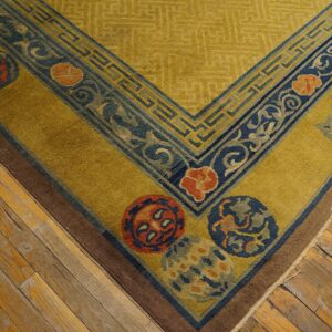 Gold rug featuring dark blue geometric borders and orange medallions rests on distressed hardwood flooring.