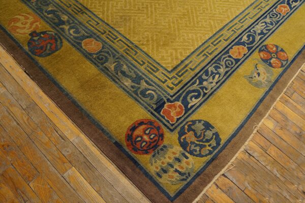 Gold rug featuring dark blue geometric borders and orange medallions rests on distressed hardwood flooring.