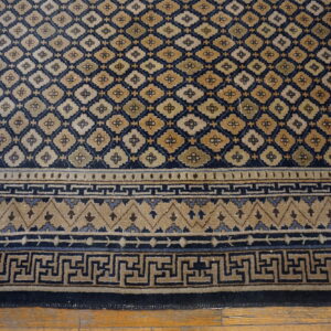 Navy blue and tan rug with a diamond lattice field and Greek key pattern border on wood planks.