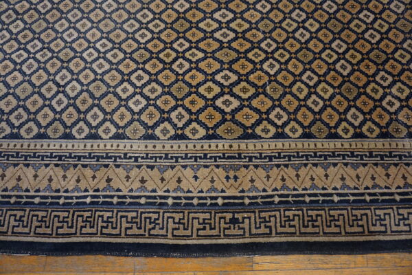 Navy blue and tan rug with a diamond lattice field and greek key pattern border on wood planks.