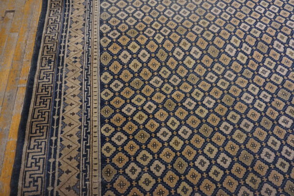 Navy and beige rug with geometric motifs and patterned borders laid over worn golden wooden planks.