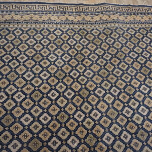 Navy and beige rug featuring an all-over geometric trellis and complex patterned borders on wooden flooring.