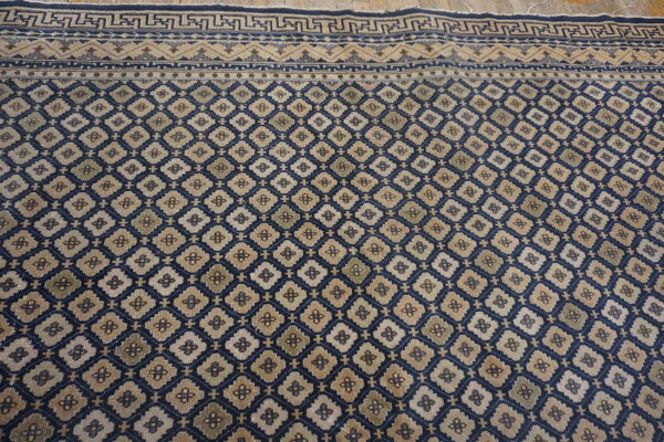 Navy and beige rug featuring an all-over geometric trellis and complex patterned borders on wooden flooring.