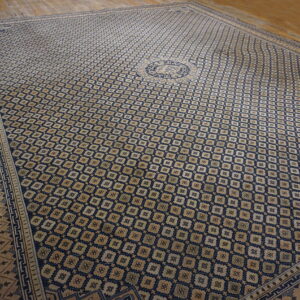 Navy and tan geometric rug with a central medallion and detailed border on light wood flooring.