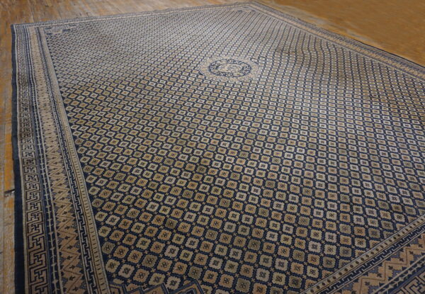 Navy and tan geometric rug with a central medallion and detailed border on light wood flooring.