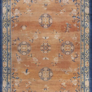 Orange rug featuring light blue and cream floral medallions, framed by a wide navy and cream border.