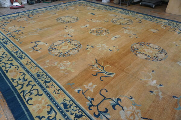Tan rug with scattered light floral motifs and a strong navy blue, yellow, and teal patterned border.