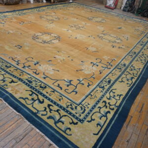 Large golden rug with scattered blue floral motifs and thick indigo borders on distressed wood flooring.