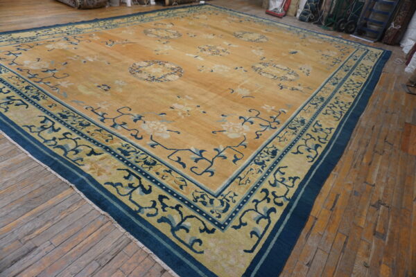 Large golden rug with scattered blue floral motifs and thick indigo borders on distressed wood flooring.