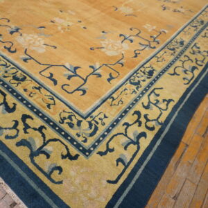 Golden yellow rug with blue floral border and center detail, resting on rustic wooden floorboards.