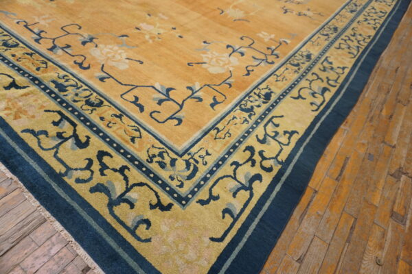 Golden yellow rug with blue floral border and center detail, resting on rustic wooden floorboards.