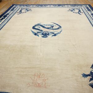 Cream rug with blue traditional dragon designs and borders rests on light wooden floorboards.