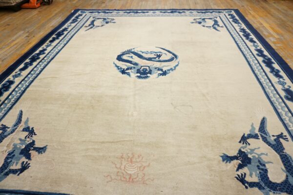 Cream rug with blue traditional dragon designs and borders rests on light wooden floorboards.