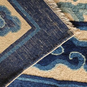 Close-up of a rug folded, highlighting its abstract blue and tan high pile next to a dark blue flatweave border.