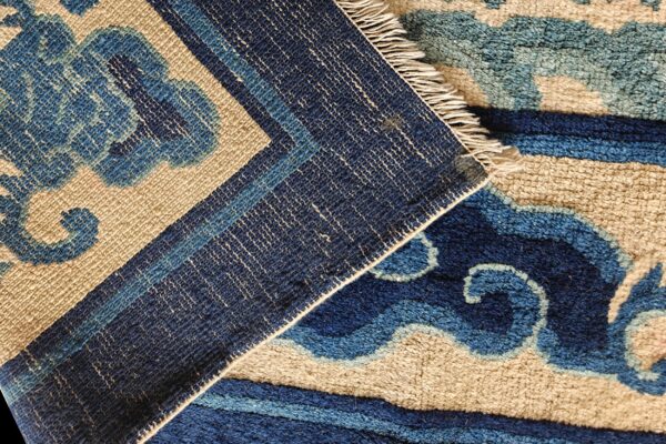 Close-up of a rug folded, highlighting its abstract blue and tan high pile next to a dark blue flatweave border.