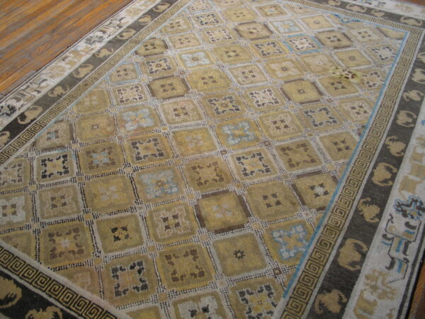 Yellow-gold rug featuring a checkered pattern, blue accents, and dark borders with greek key designs on wood flooring.