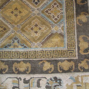 Low pile rug detail showing golden diamonds, light blue highlights, and a border of dark Greek keys.