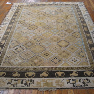 Beige, gold, and dark brown rug with a geometric diamond pattern covers wide plank wood flooring.