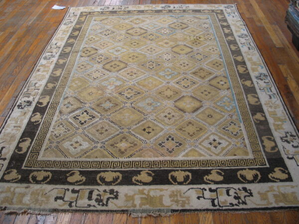 Beige, gold, and dark brown rug with a geometric diamond pattern covers wide plank wood flooring.