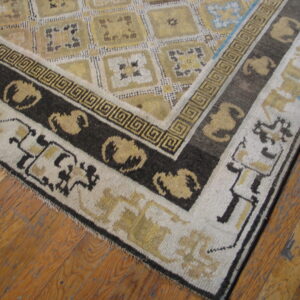 Geometric gold, cream, and dark brown rug corner features a Greek key border on wood planks.