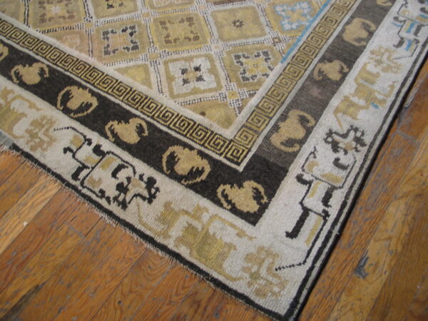 Geometric gold, cream, and dark brown rug corner features a greek key border on wood planks.
