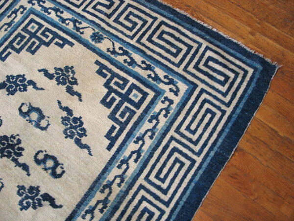 A cream and blue rug with a dense greek key border pattern rests on warm brown hardwood flooring.