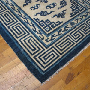 Cream rug with thick dark blue key pattern border and cloud motifs on wood floor.