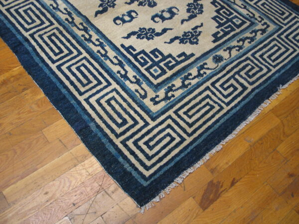 Cream rug with thick dark blue key pattern border and cloud motifs on wood floor.