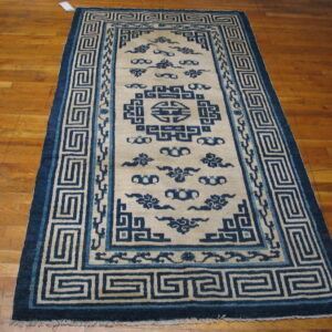Blue and cream rug with geometric borders and cloud designs covering a wood plank floor.