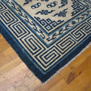 Blue and cream rug featuring geometric key and stylized cloud patterns on light brown wood flooring.