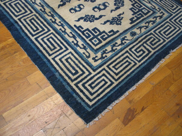 Blue and cream rug featuring geometric key and stylized cloud patterns on light brown wood flooring.