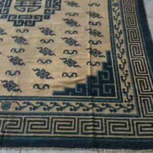 Tan rug featuring dark blue meander borders and scrolling cloud motifs on a gray tile background.