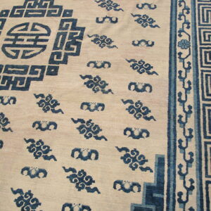 Close-up of a low-pile cream rug with deep blue geometric and cloud patterns, featuring a Greek key border.