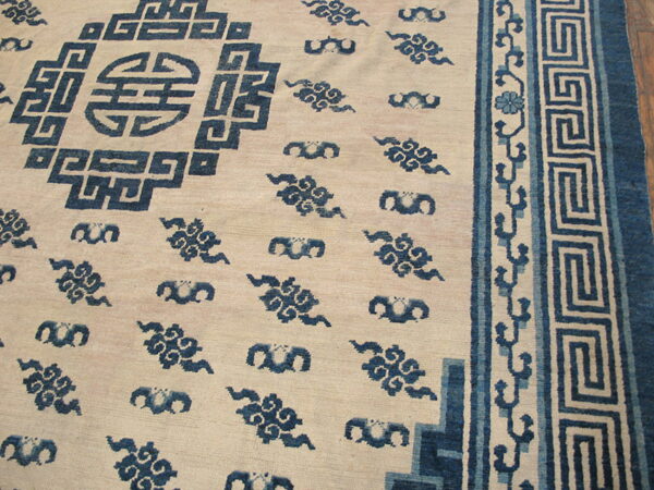 Close-up of a low-pile cream rug with deep blue geometric and cloud patterns, featuring a greek key border.
