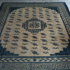 Tan and dark blue rug with a central medallion, scattered cloud motifs, and a Greek key border on tile.