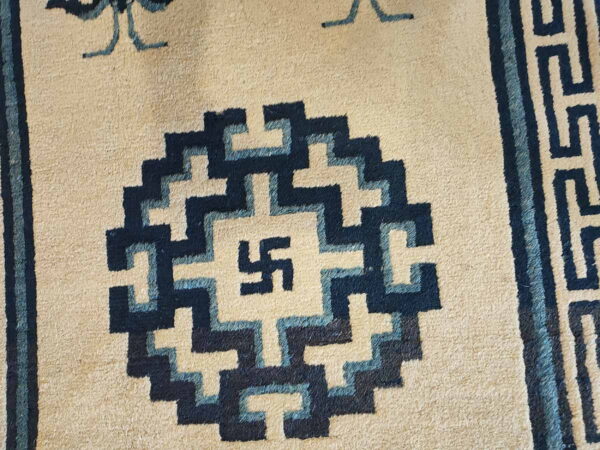 Beige rug featuring a detailed dark and light blue stepped pattern surrounding a central swastika design.