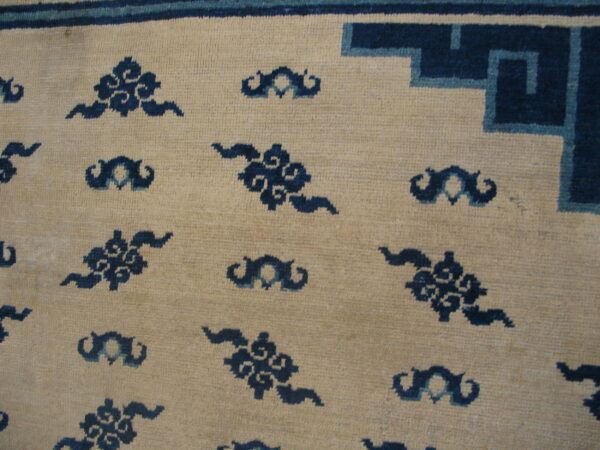 Low-pile beige rug with dark blue cloud motifs and a blue and light blue geometric corner border.