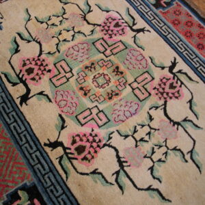 Beige field rug with vibrant pink florals, teal geometric shapes, and black outlining on a wood floor.