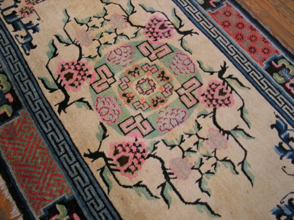 Beige field rug with vibrant pink florals, teal geometric shapes, and black outlining on a wood floor.