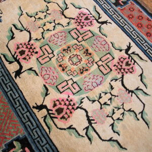 Beige rug featuring pink floral sprays, a central geometric motif, and blue meander borders on wood floor.