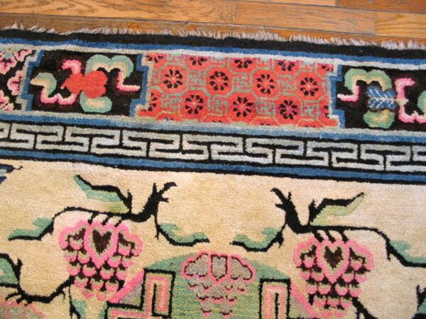 Multicolored rug border with geometric and floral patterns in pink, black, blue, and cream on hardwood.