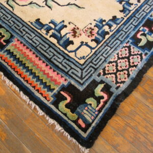 Detailed view of a beige rug corner bordered by complex blue, black, pink, and orange patterns on a wood floor.