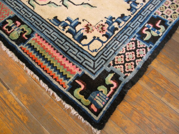 Detailed view of a beige rug corner bordered by complex blue, black, pink, and orange patterns on a wood floor.