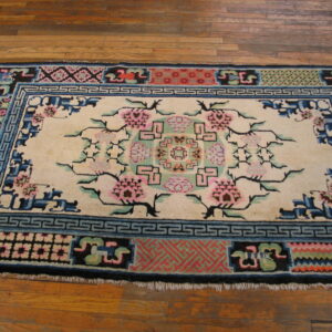 Cream rug with pink floral motifs and elaborate blue and black borders rests on a hardwood floor.