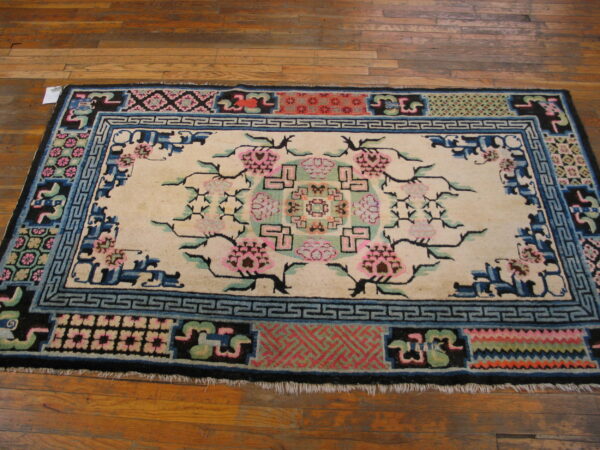 Cream rug with pink floral motifs and elaborate blue and black borders rests on a hardwood floor.