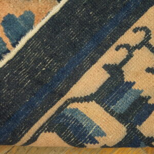 Textured rug in peach, navy, and blue is folded over, revealing the woven backside on wood planks.