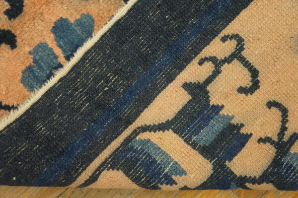 Textured rug in peach, navy, and blue is folded over, revealing the woven backside on wood planks.