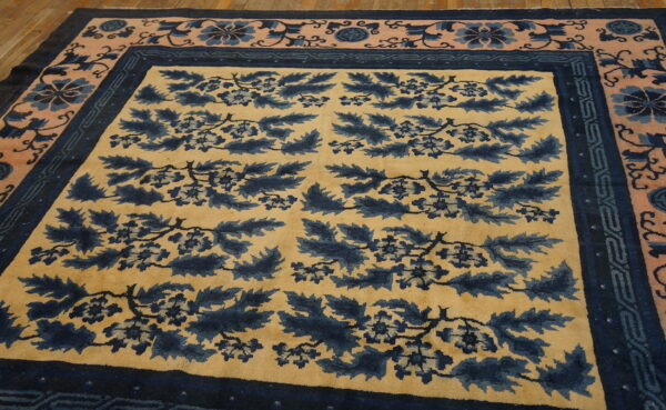 Yellow field rug with large navy floral designs, framed by blush pink and dark blue borders on wood planks.